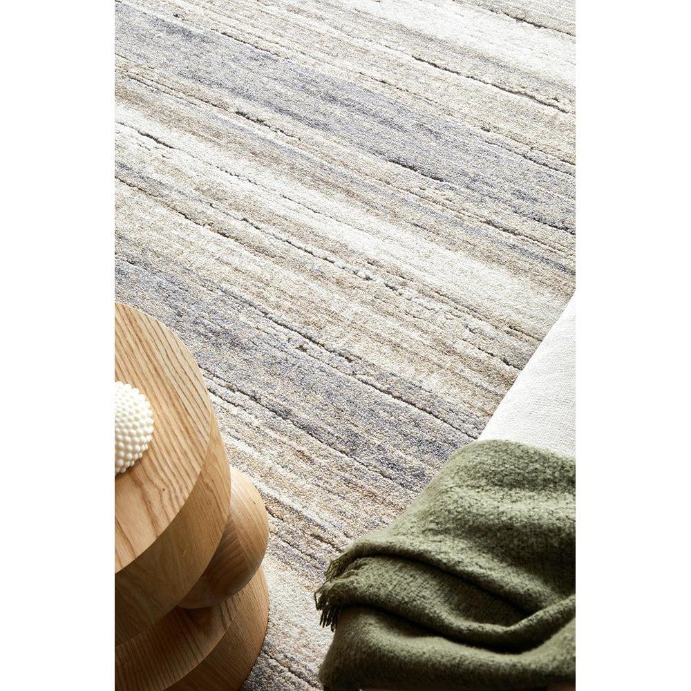 Textured area rug with a wooden side table and green blanket on a neutral background