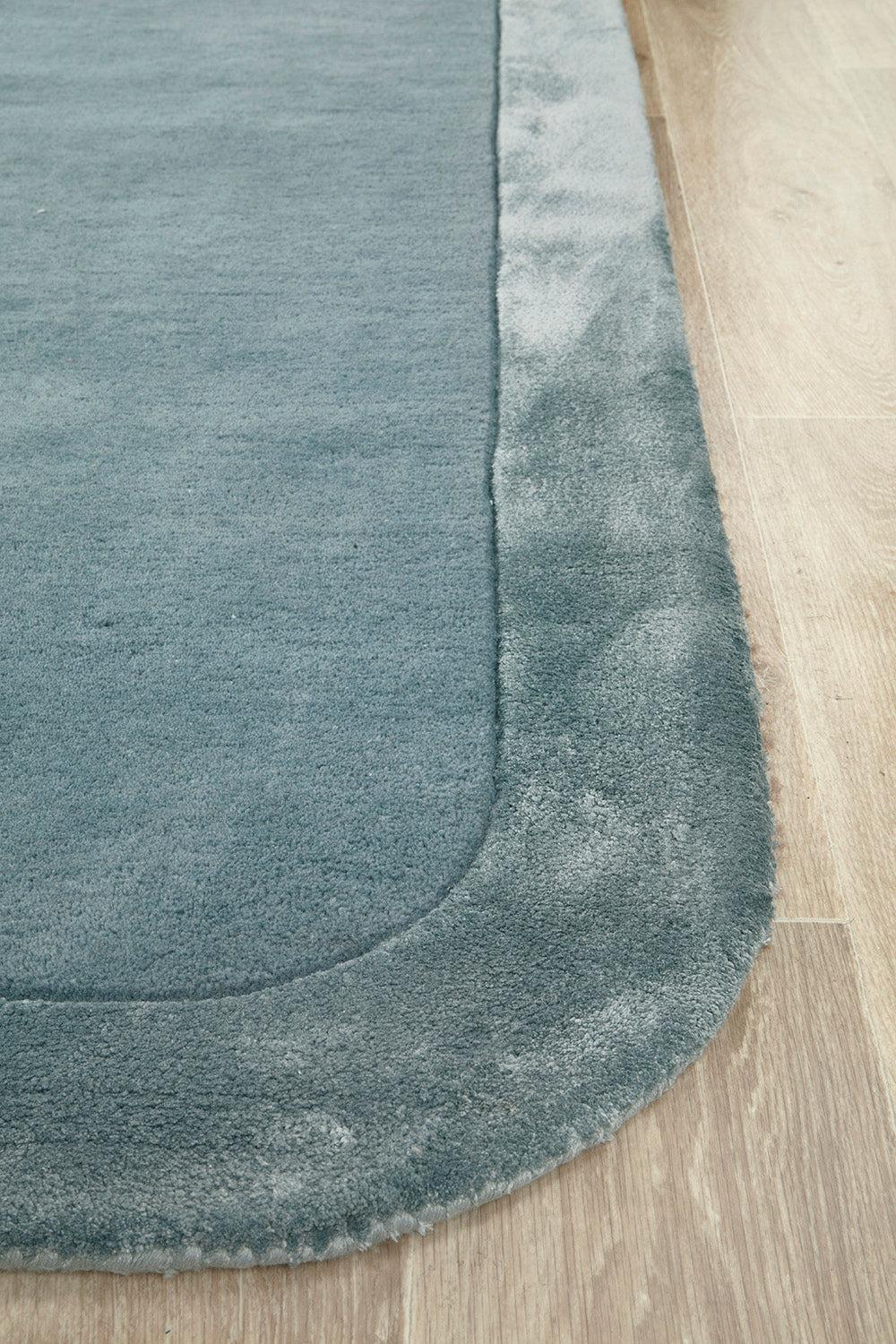 Hugo Rug featuring solid blue field with darker blue edge on light wooden floor; construction and material unspecified