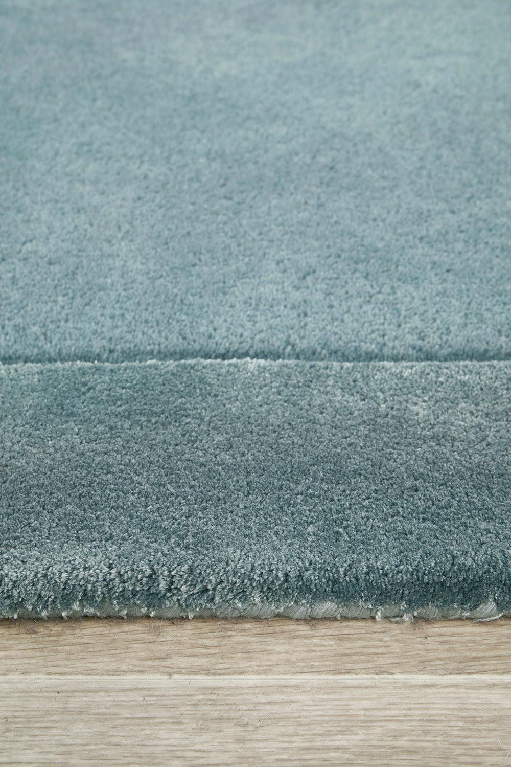 Hugo Rug featuring solid textured pattern in steel blue, dusty blue and teal on light wood floor, hand-tufted wool