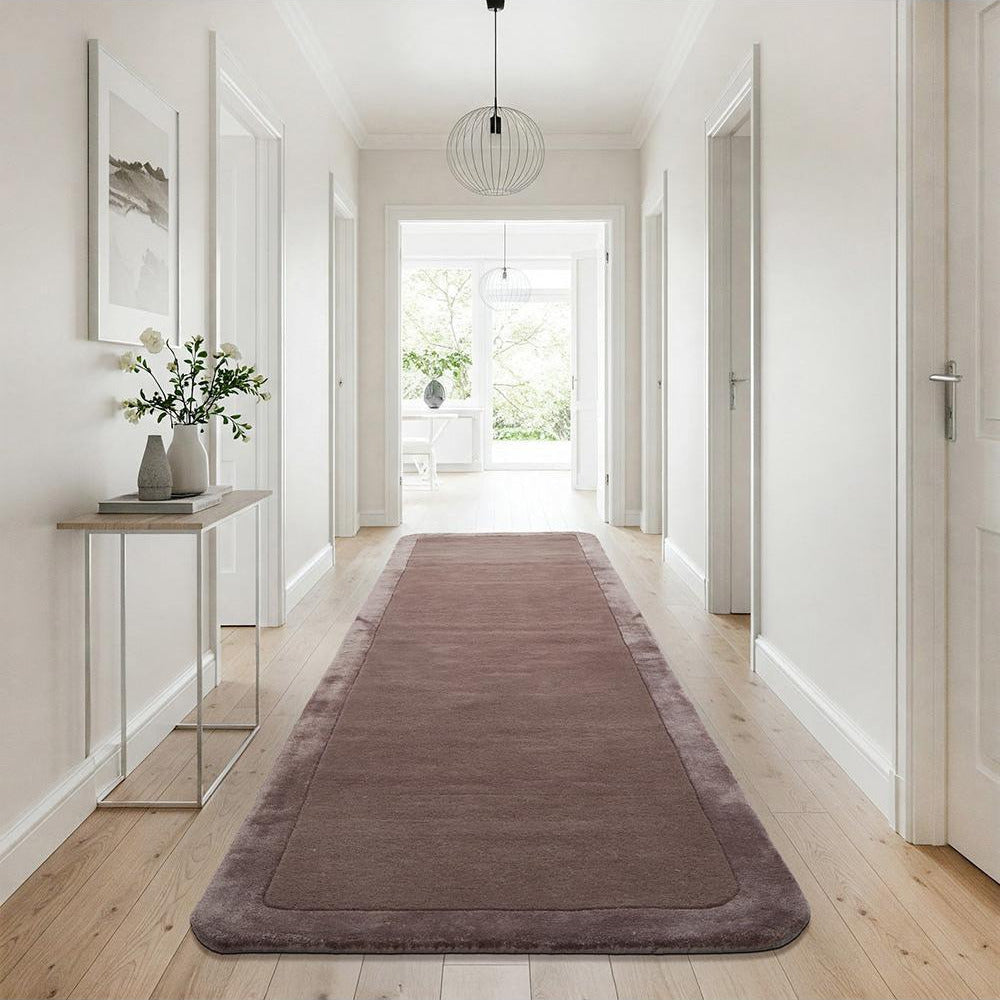 Brown runner rug on a wooden floor in a bright hallway with white walls and a glass door.
