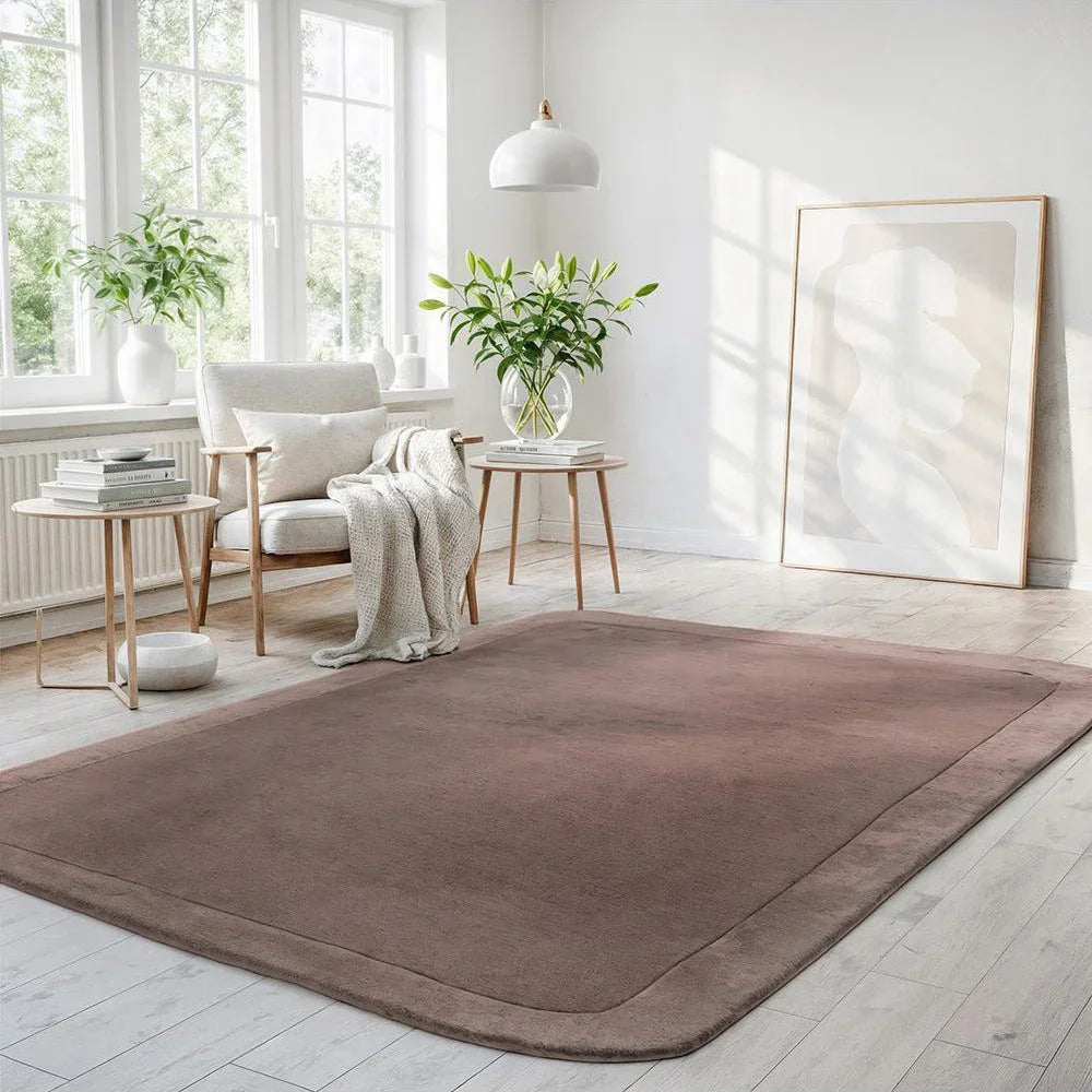 Brown rug on a light wooden floor with a white wall and window in the background