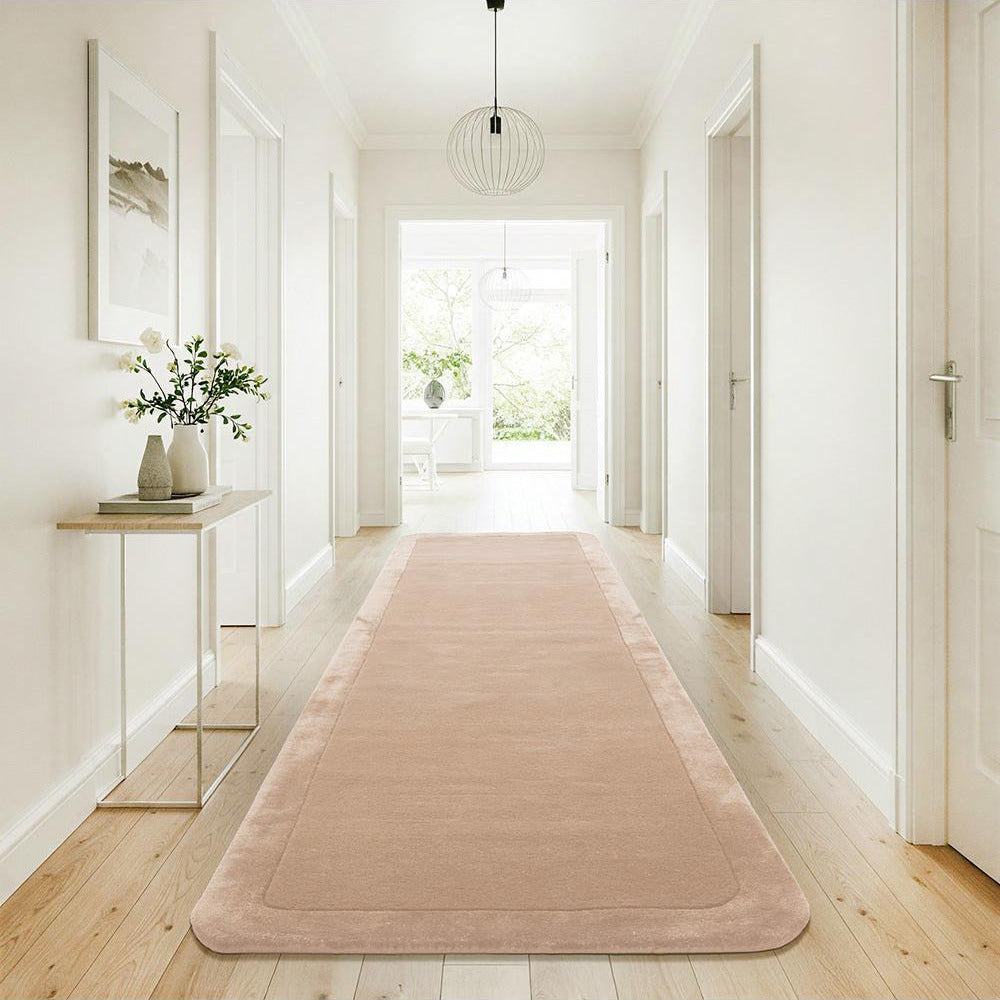 Pink runner rug on a wooden floor in a bright hallway with white walls and a glass side table.