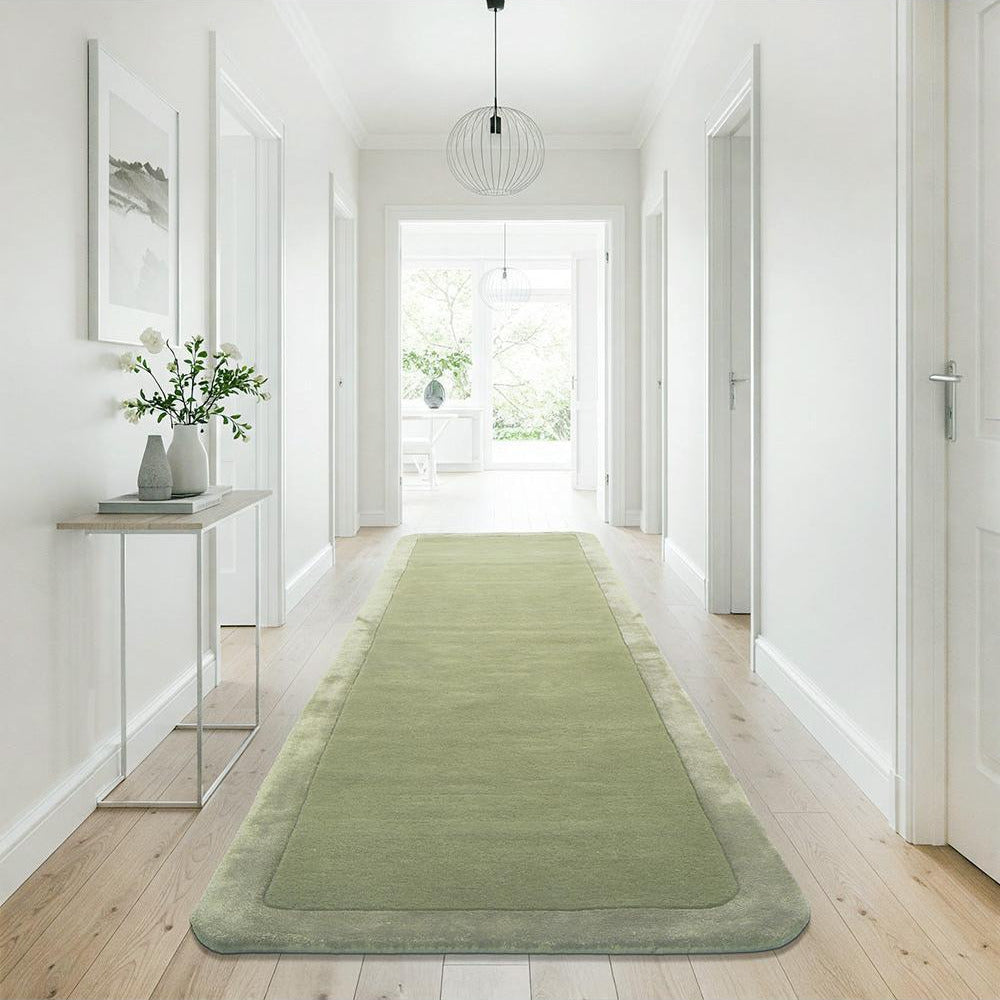 Green runner rug on a wooden floor in a bright hallway with white walls and a glass side table.