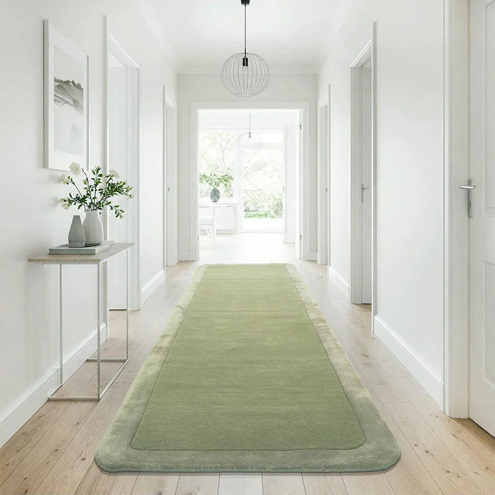 Green runner rug on a wooden floor in a bright hallway with white walls and a glass side table.