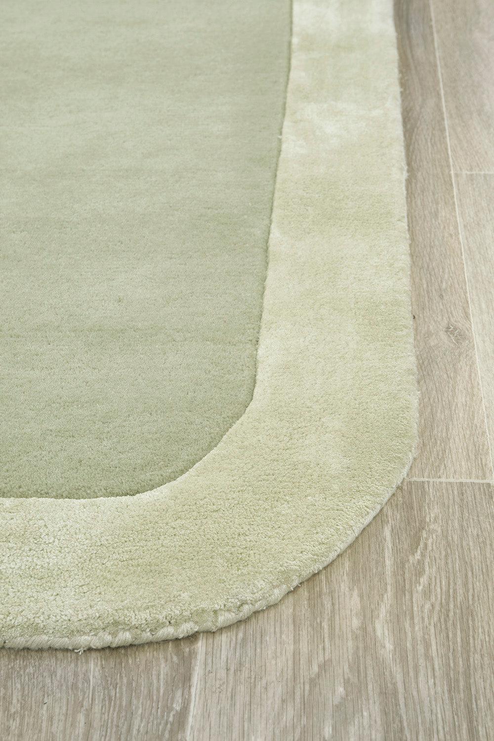 Hugo Sage Rug featuring solid sage green with cream border on light wood floor, machine-woven wool