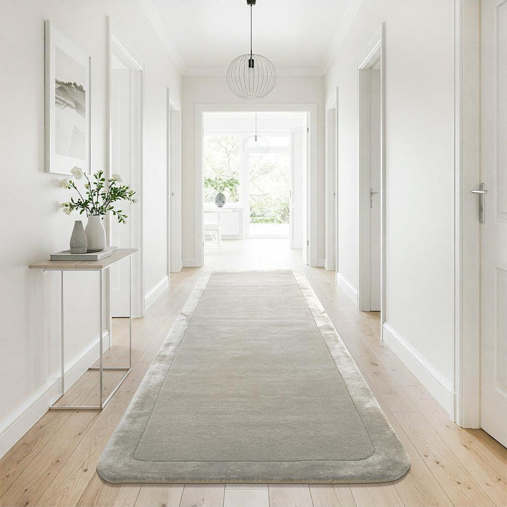 Long rectangular rug on a wooden floor in a bright hallway with white walls and a light fixture.