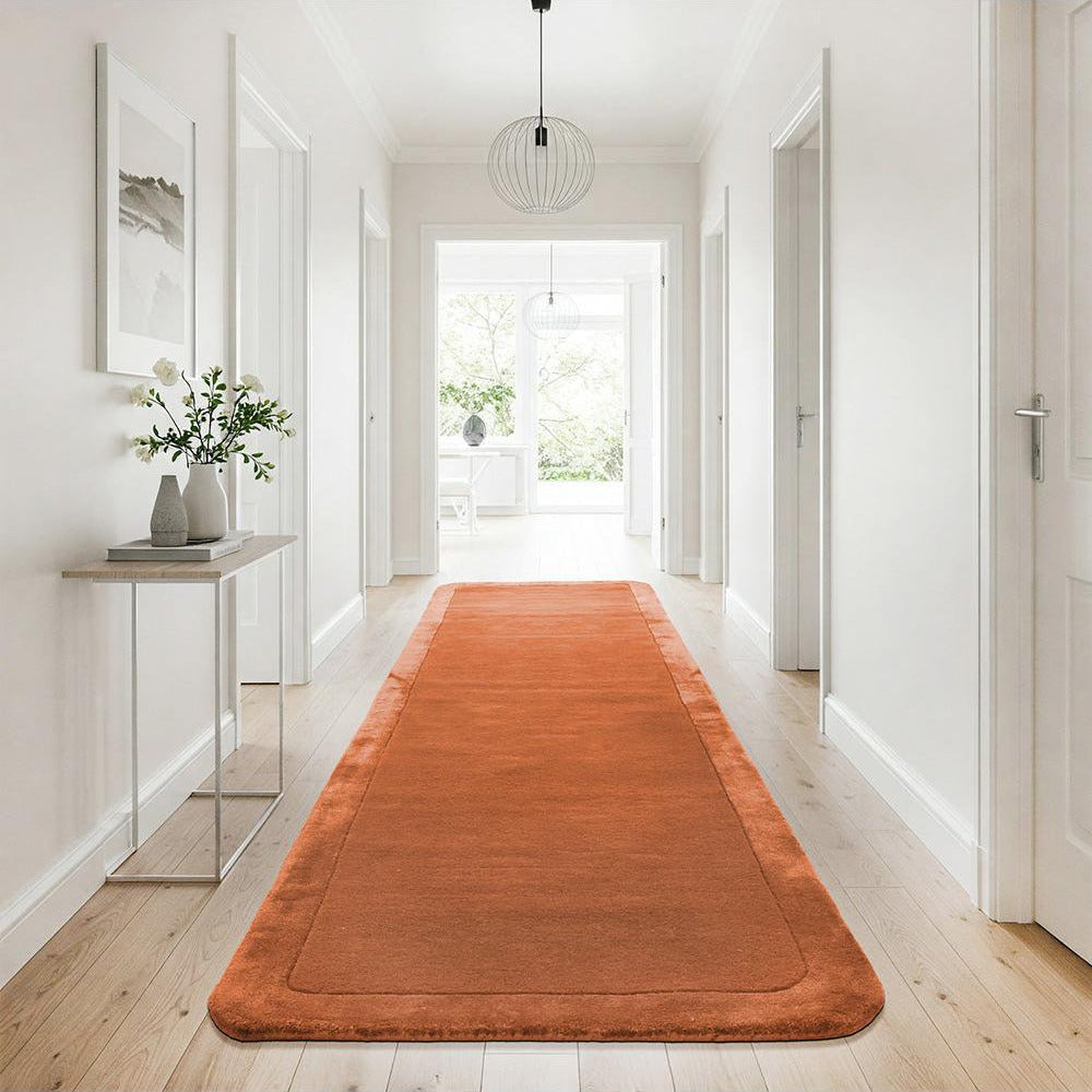 Orange runner rug on a wooden floor in a bright hallway with white walls and a glass side table.