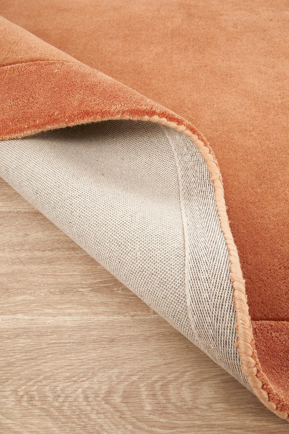 Hugo Spice Rug featuring solid textured pattern in terracotta spice and beige on natural wood, machine-woven wool