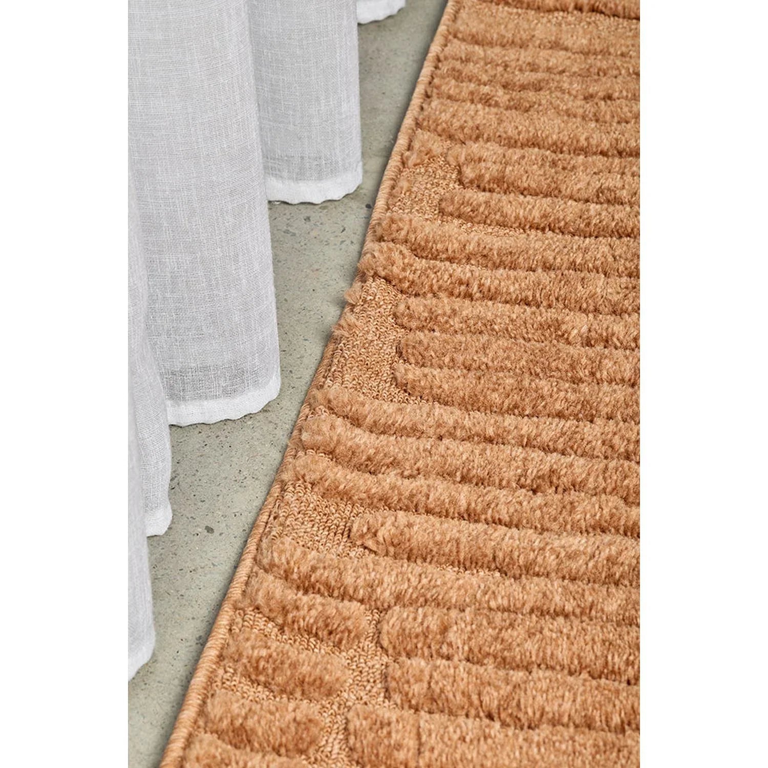 Haven Aliya Rust Runner Rug featuring textured ribbed pattern in rust and terracotta on grey concrete floor, hand-tufted wool