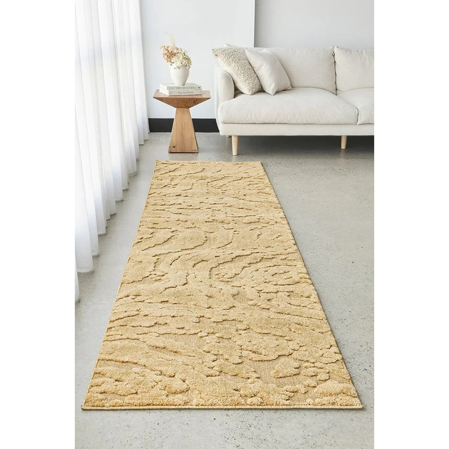 Beige textured rug on a light gray floor in a living room setting with a sofa and side table.