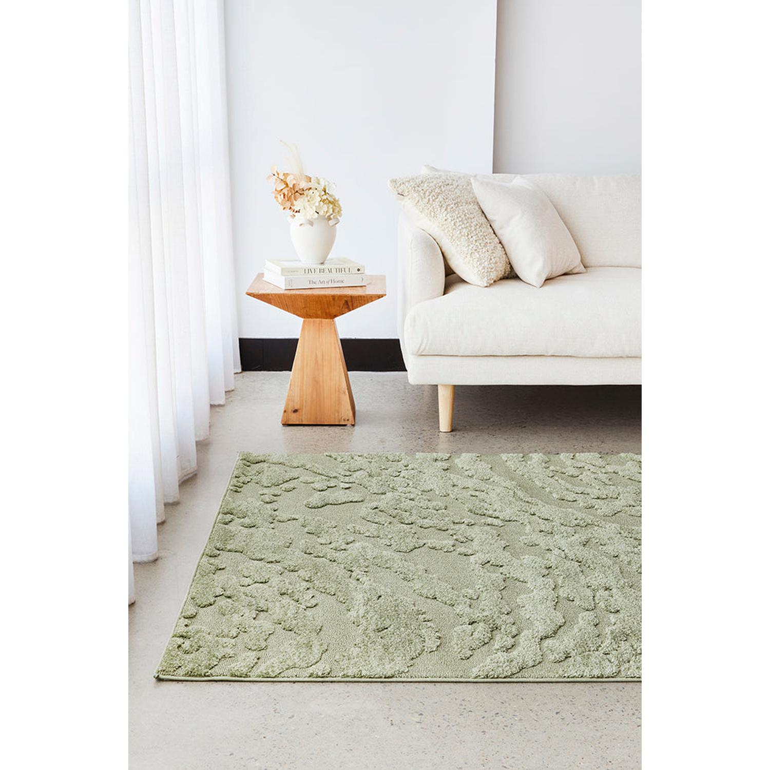 Green rug on a light gray floor with a white sofa and wooden side table in the background.