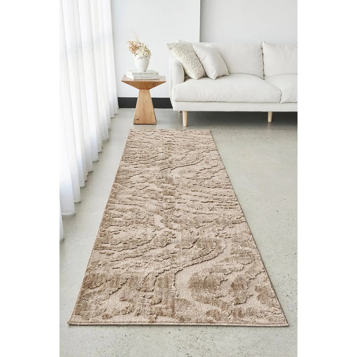 Beige runner rug on a light gray floor in a living room setting with a white sofa and small wooden table.