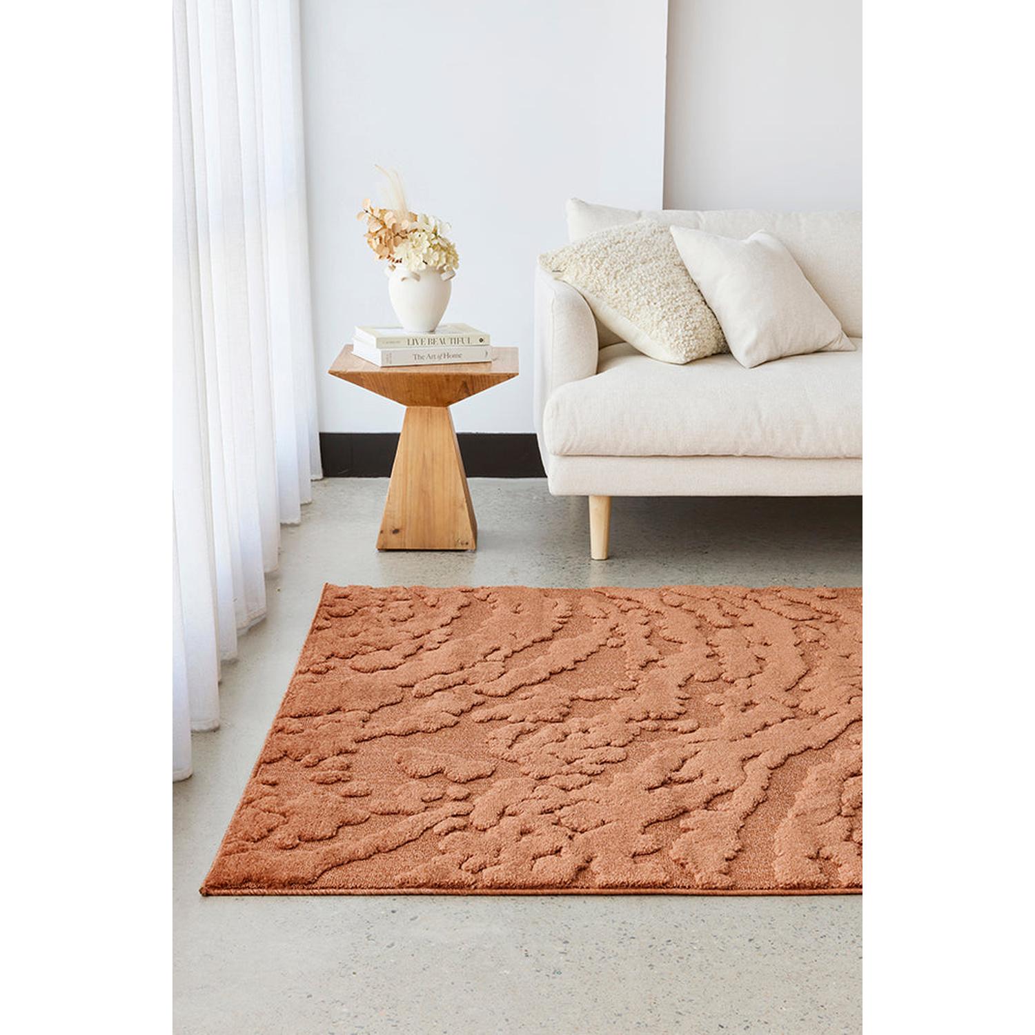 Living room with a textured orange rug, white sofa, and wooden side table.