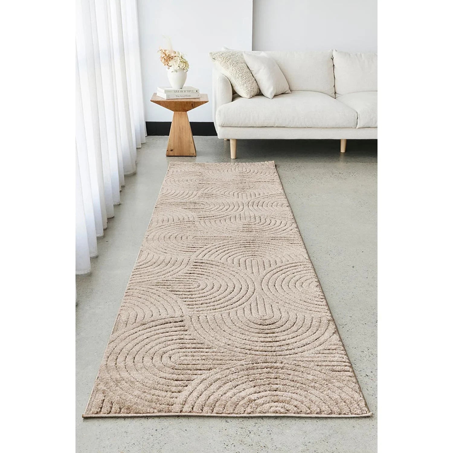 Beige patterned rug on a concrete floor with a white sofa and wooden side table in the background.