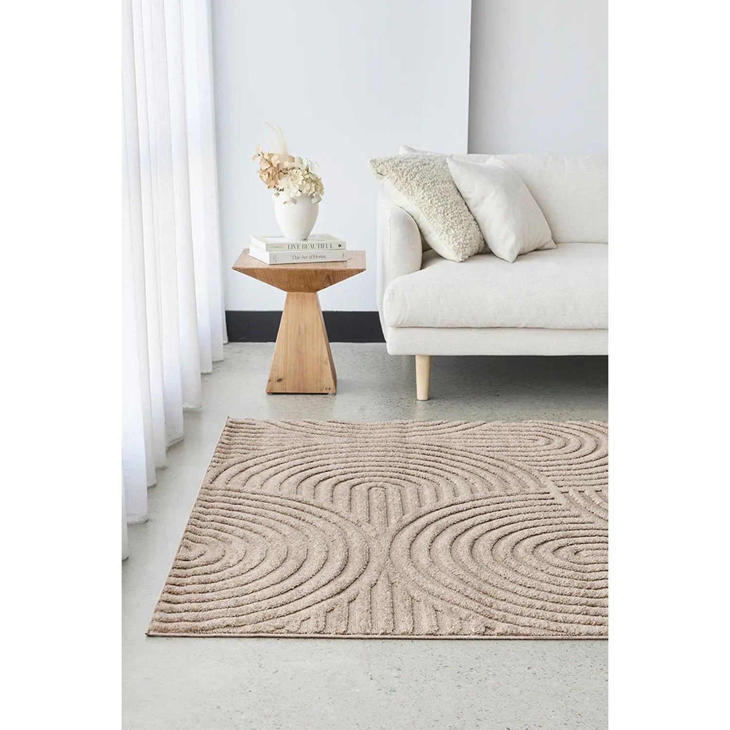Living room with a beige textured rug, white sofa, and wooden side table.