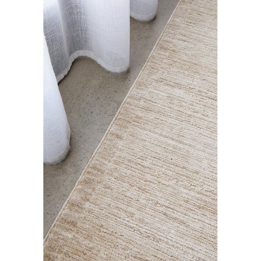 Steph And Gian Birch Flax Rug featuring understated striped pattern in beige, cream and tan on light grey concrete, hand-loomed flax