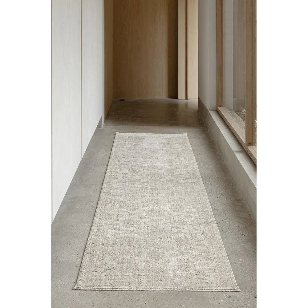 Long rectangular rug on a concrete floor with wooden walls and a window.