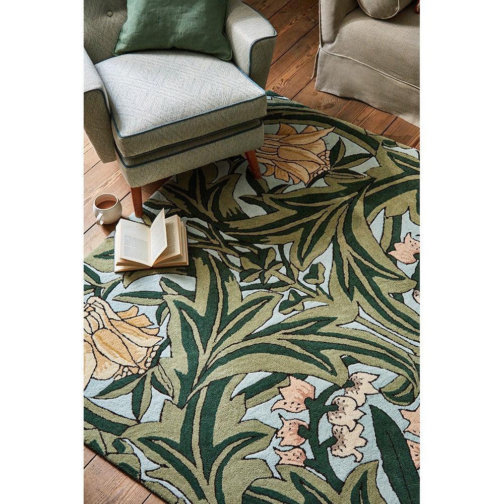 Morris & Co Bluebell Leafy Arbour Green rug featuring botanical leafy pattern in emerald, olive, sage, peach on light blue background, hand-tufted wool
