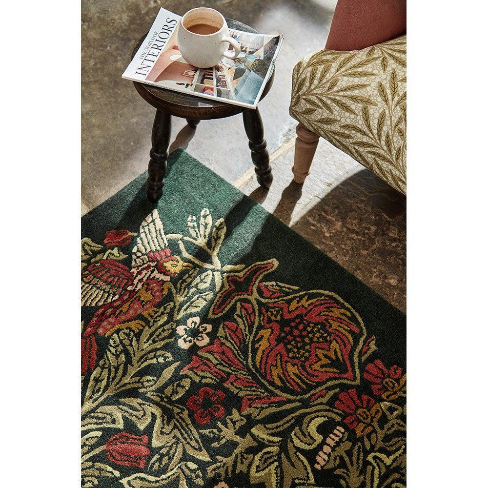 Morris & Co Bird Tump Green Designer Rug featuring floral pattern in red, cream, gold and olive on dark green background, hand-tufted wool