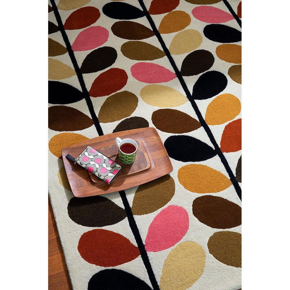 Orla Kiely Multi Stem Autumn Designer Rug featuring botanical leaf stem pattern in mustard, brown, black and pink on cream background, hand-tufted wool