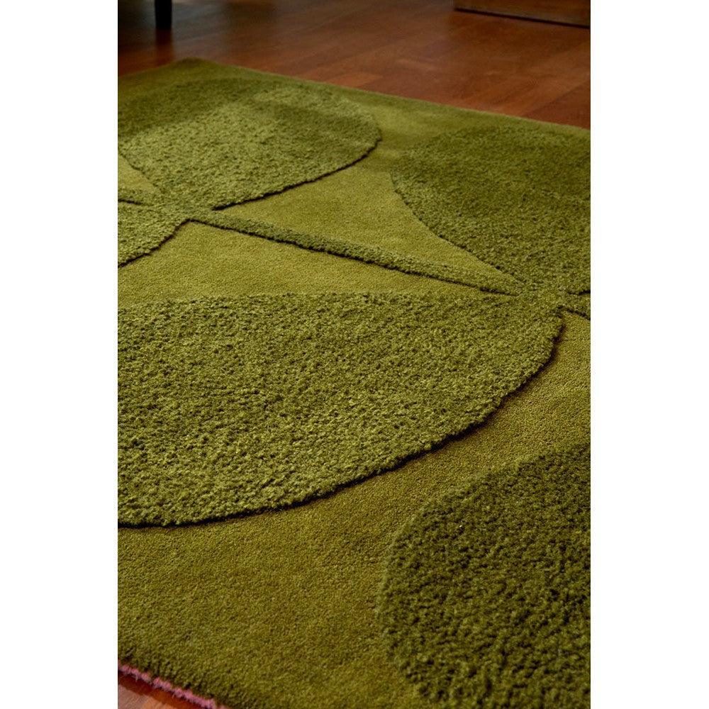 Orla Kiely Solid Stem Fern Designer Rug featuring circular geometric pattern in olive, moss, lime greens with pink accents on brown floor, hand-tufted wool