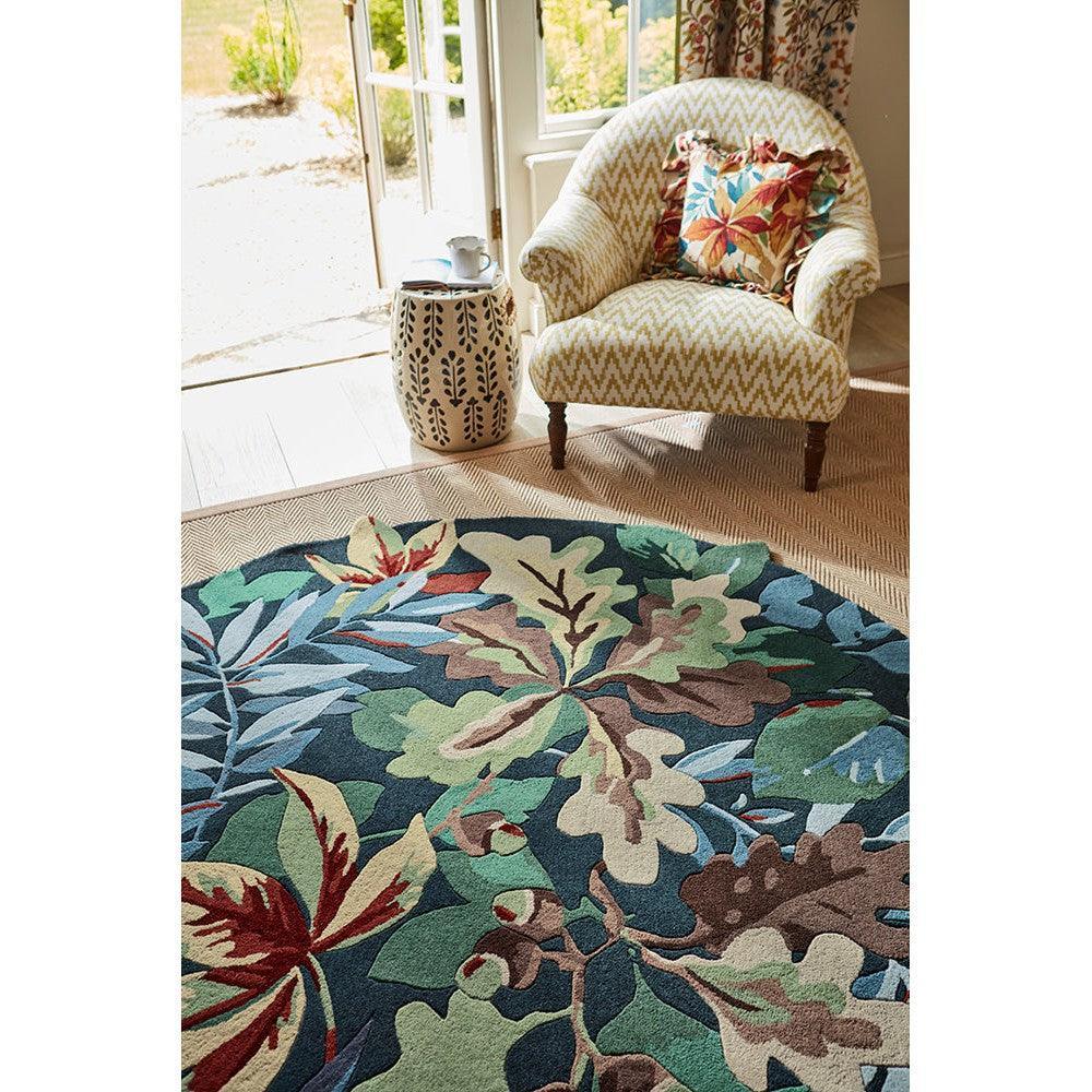 Sanderson Robin's Wood Round Designer Rug featuring botanical leaf pattern in forest green, teal, sage and cream on navy background, hand-tufted wool
