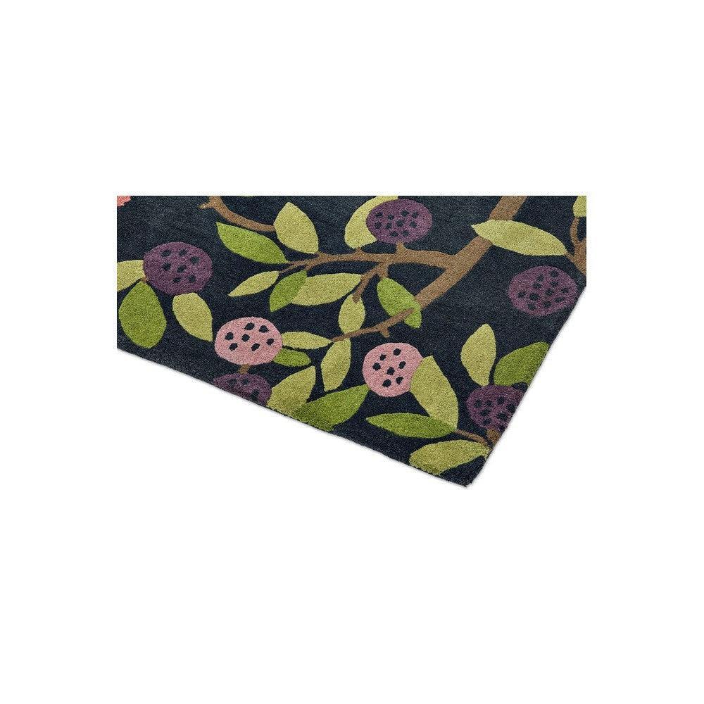 Sanderson Foraging Indigo Rug featuring botanical leaves and berries in navy, lime green and pink on a dark background, hand-tufted wool