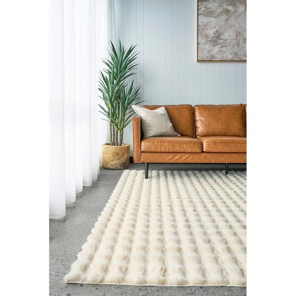 Bubble Natural machine washable rug featuring bubble-textured cream pile on a light blue living room with a tan leather sofa.