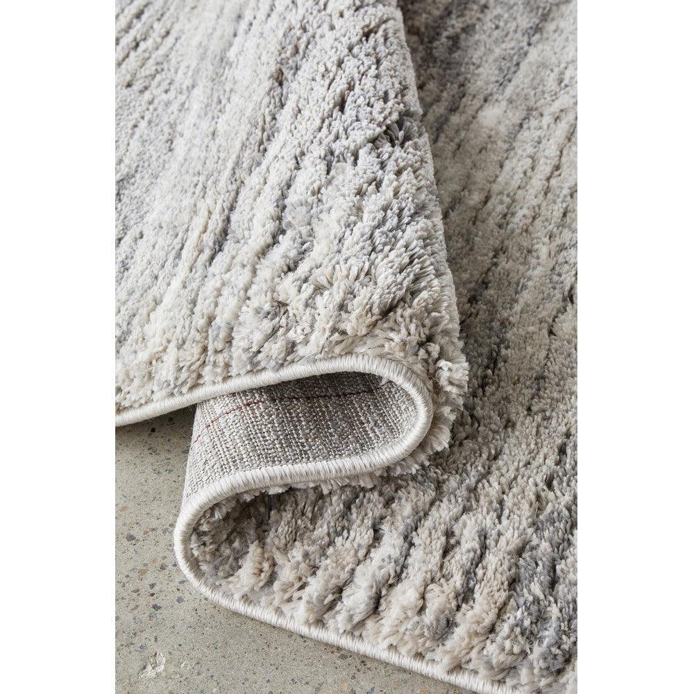 Himali Fin rug featuring shaggy pile in steel grey, ivory and beige on light concrete background, machine-made wool