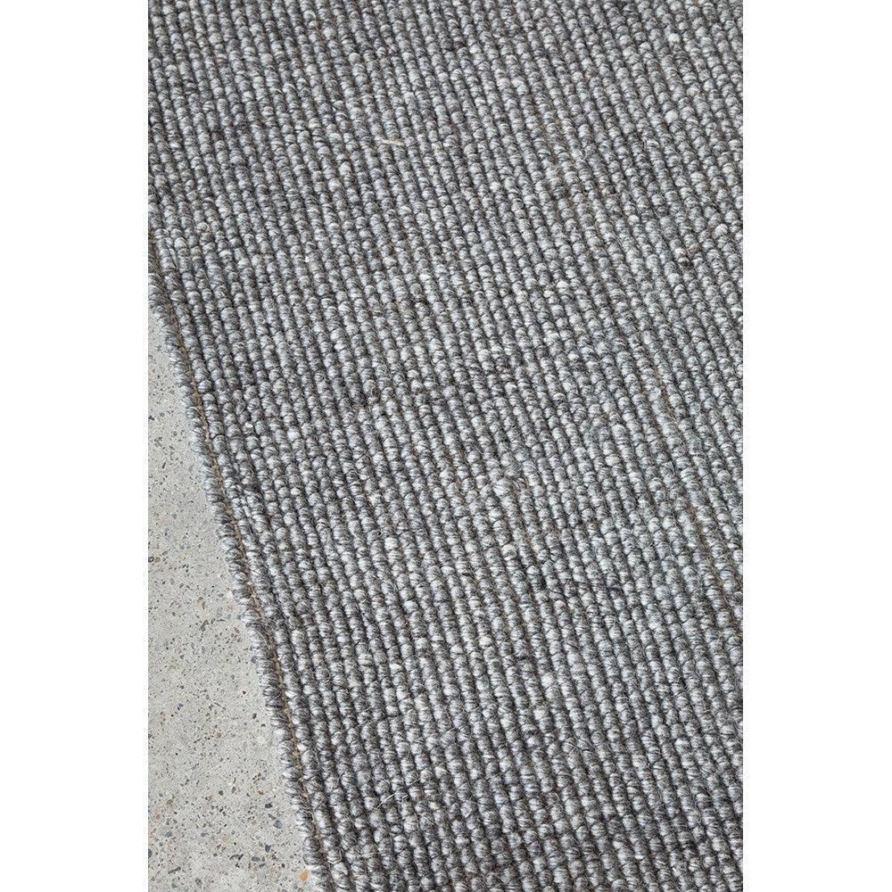 Harlow Ariel Graphite Rug featuring ribbed texture in graphite, charcoal, silver grey on light concrete background, hand-tufted wool